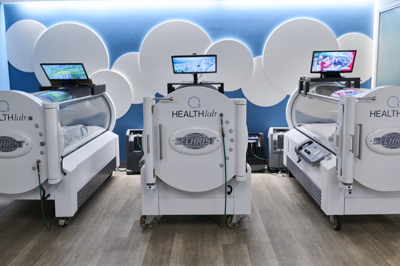 Three clear, medical-grade hyperbaric chambers at O2 Health Lab, each with its own screen